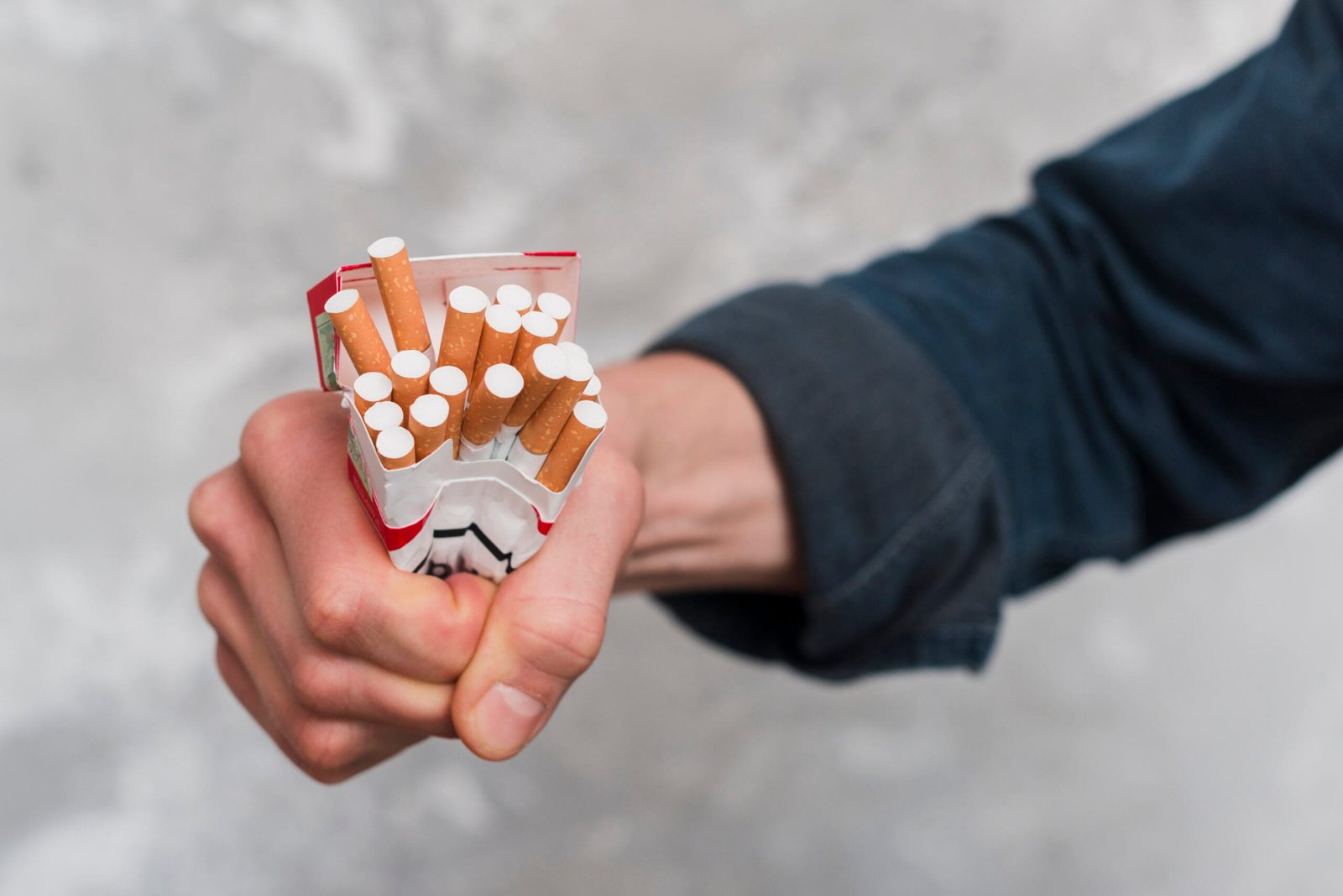 close up man s hand crushing cigarettes box scaled